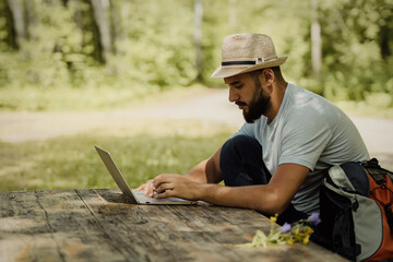 A person man with backpack working on laptop outdoors sitting at the wooden antique desk. Concept of travel, freelance, business.