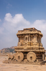 Naklejka premium Hampi, Karnataka, India - November 5, 2013: Vijaya Vitthala Temple. Brown stone chariot protrait under blue cloudscape.