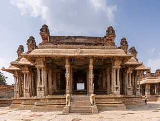 Fototapeta premium Hampi, Karnataka, India - November 5, 2013: Vijaya Vitthala Temple. Looking straith through brown stone sanctuary with hollow pillars under blue cloudscape.