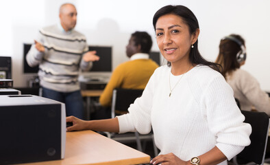 Smiling Latina engaged in self-education using pc for searching information in public library