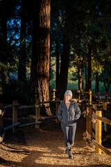 Woman walking through Redwood Forest in Park with Warm Cloths at Sunset