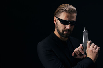 Portrait of dangerous gangster in sunglasses holding real weapon while posing in studio with black background. Criminal lifestyle.