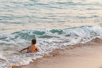 A little boy learns to swim by the sea on weekends. The wave comes to the beach.