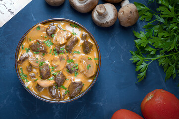 Traditional beef stroganoff with cream of champignon mushrooms in a blue bowl with its ingredients seen from above