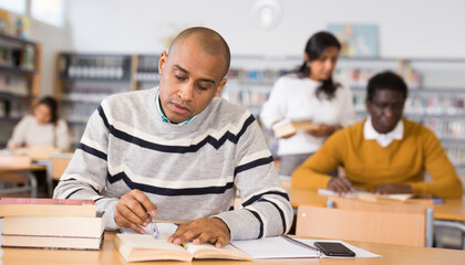 Young adult man working with books, finding information at library