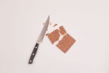 Milk chocolate with nuts lies broken near a knife on a white background. Top view. Place for an...