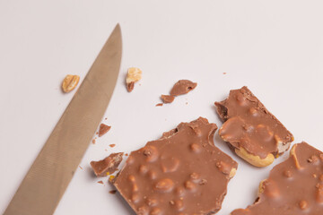 Milk chocolate with nuts lies broken near a knife on a white background. Top view. Place for an inscription. Advertising. Close plan. Food. Sweets