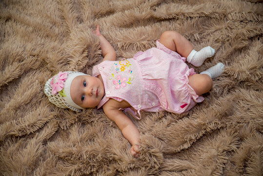 A girl in a pink dress and a cap with a flower rests on a brown plaid