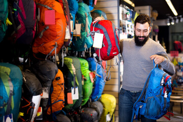 Smiling guy deciding on new rucksack in sports equipment store