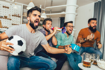 Happy male friends with vuvuzela wearing black face protective mask watching football at home