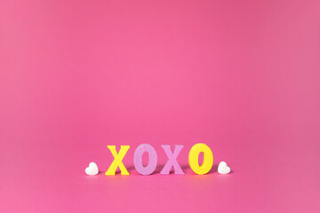 XOXO word in yellow and purple colors with white hearts on pink background. Love, hugs and kisses, Valentine Day greeting card with copy space.