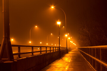 A night shot with ambient street lamp light during a foggy night of a road and a bridge with low...