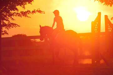 SIlhouette of young girl riding horse over low jumps