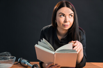 Excited female is going to cook something special, reading cookbook.