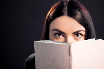 Beautiful brunette girl looking from behing the book in pink cover.