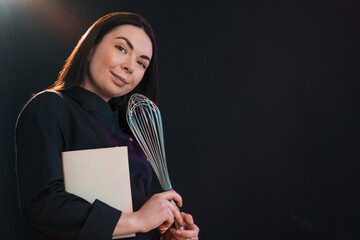 Exited female is going to cook, holding a cookbook and eggbeater.