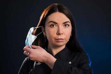 Closeup portrait of woman taking off her medical mask over black background.