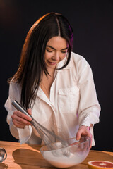 Young smiling female whisking raw eggs in bowl, cooking breakfast.