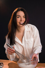 Young smiling female whisking raw eggs in bowl, cooking breakfast.