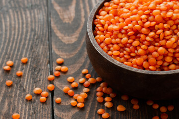 Uncooked raw red lentil in wooden shovel or bowl on wooden background, (Lens culinaris)
