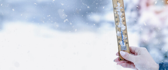 A young adult woman hold in her hand snowy thermometer showing a temperature slightly below...