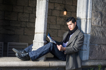 A young guy is sitting on a old window frame and reading.