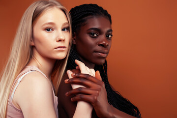 two pretty girls african and caucasian blond posing cheerful together on brown background, ethnicity diverse lifestyle people concept