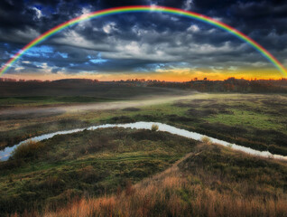 Amazing rainbow over the small rural river. autumn morning

