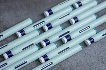 Dynamic row of syringe self application pens on rustic textured gray background. Studio medical equipment still life concept with auto-injector disposable devices. © Maarten Zeehandelaar
