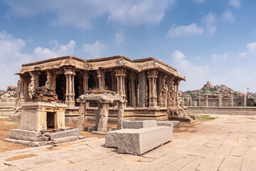 Fototapeta premium Hampi, Karnataka, India - November 5, 2013: Vijaya Vitthala Temple. ruinous structures such as mandapam and others under blue cloudscape. Boulder hills on horizon.