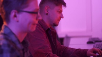 Two men high-five each other and play video games in a dark room. Esports. Competitions in a video game. - Powered by Adobe