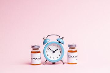 abstract vaccine vials and bottles for injection over pink background. alarm clock near vaccination...