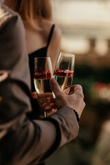 Love couple staying together and holding glasses with sparkling champagne and red heart shaped confetti. The concept of wedding, lovers day. Happy Valentines day celebration concept. Close up