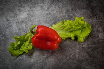 Red sweet Bulgarian pepper on green lettuce leaves on a colorful background