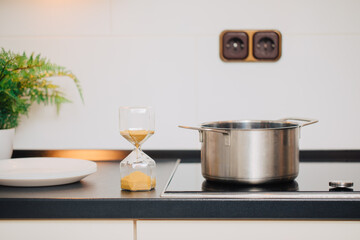kitchen utensils on the kitchen table. Hourglass is on the kitchen table next to a plate and a saucepan. Time in the kitchen. Time to prepare the meal