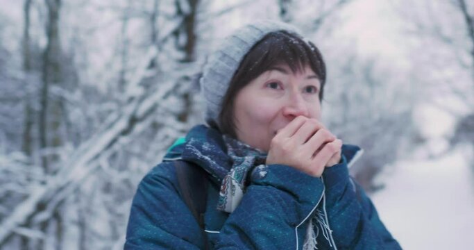 Woman warms her cold hands with breath Fun in snowy winter forest. Woman laughs as she walks through wood. Sincere emotions.