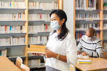 Portrait of adult latin american woman in protective face mask visiting public library during coronavirus pandemic. Concept of compelled precautions..