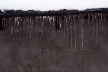 house roof with snow and icicles with unfocused grey wall background  - winter close up, frozen backdrop