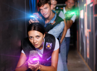 Group happy emotional people with laser guns playing laser tag game together in dark corridor