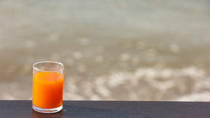 A glass of orange juice put on a terrace or wooden bar with sea wave or water as background