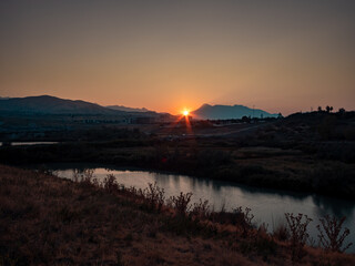 The sun shines between the mountains an lights up the valley and river