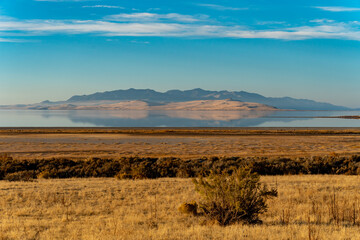 Panoramic view of grasslands, a lake and a mountain across the lake reflecting on the water