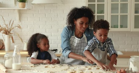 African mother little adorable son and daughter wear aprons cooking together in kitchen, using cookies cutters preparing hand-made biscuits. Hobby, cookery, happy motherhood, kids development concept