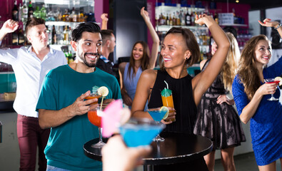 adult happy male with female are talking and drinking cocktails on the party in club