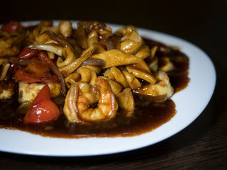 Dish of traditional Chinese cuisine Japanese tofu with vegetables and seafood on a white plate, dark background.
