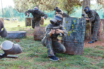 Female paintball player in camouflage and mask aiming with gun in shootout outdoors