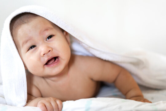 Portrait of happy smile asian baby boy relaxing looking at camera under towel after bath. Cute asian newborn child on the bed at home