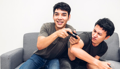 Two friends sitting on sofa and having fun enjoying play console video game together at home