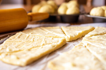 Rolling out raised yeast dough for crescent rolls.  Dough has been lathered in butter.  Wood rolling pin in background.  Dough on parchment paper.  Additional rolls in background.
