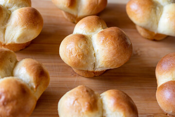Freshly baked clover dinner rolls sit cooling on a bamboo cutting board.